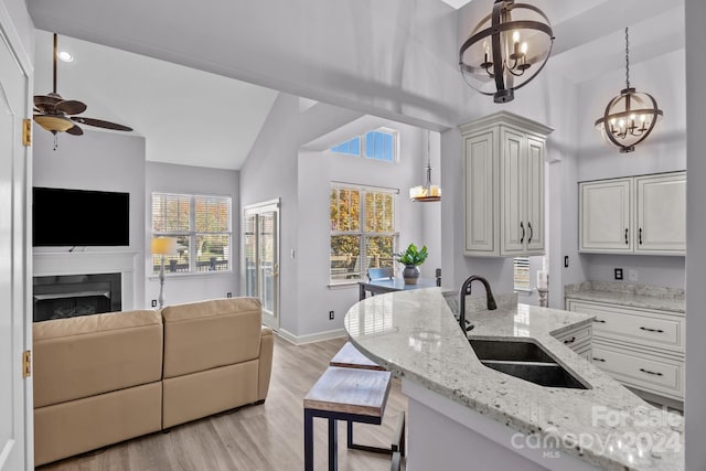 kitchen featuring light stone countertops, light wood-type flooring, ceiling fan with notable chandelier, sink, and decorative light fixtures