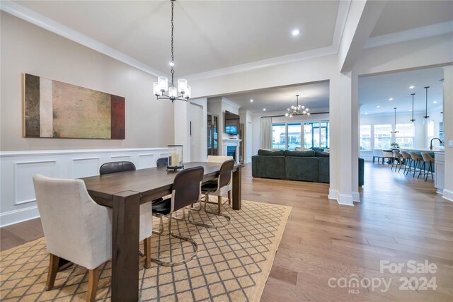 dining room with light hardwood / wood-style flooring, sink, crown molding, and an inviting chandelier