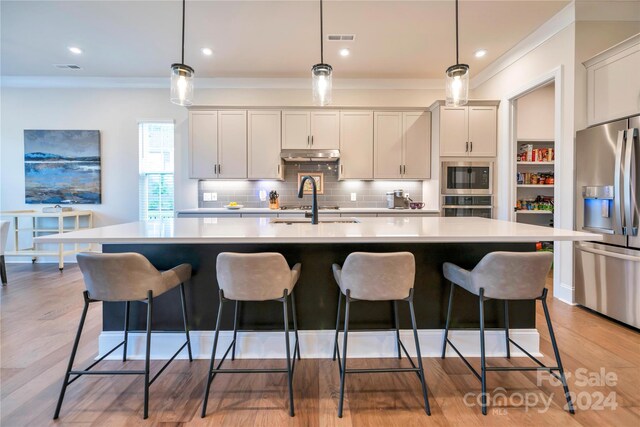 kitchen featuring hanging light fixtures, light hardwood / wood-style floors, a kitchen island with sink, and appliances with stainless steel finishes