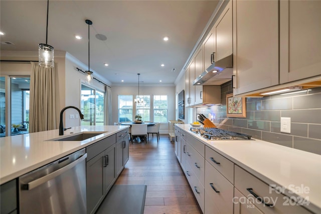 kitchen with stainless steel appliances, sink, ornamental molding, pendant lighting, and dark hardwood / wood-style flooring