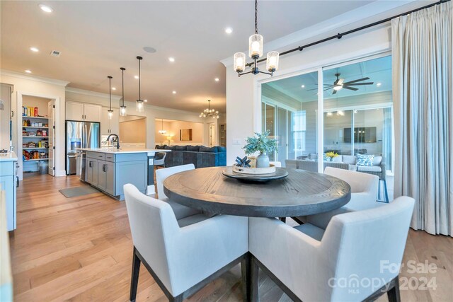 dining area with sink, ceiling fan with notable chandelier, crown molding, and light hardwood / wood-style flooring