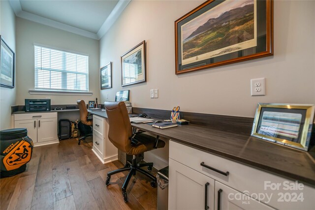 office with dark wood-type flooring, built in desk, and crown molding