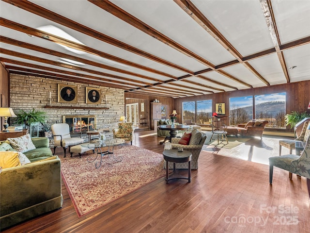 living room featuring beam ceiling, wood-type flooring, a fireplace, and wooden walls