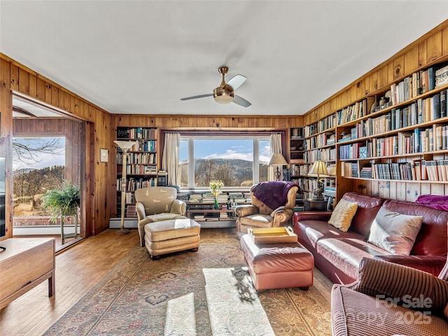 living area featuring baseboard heating, wooden walls, hardwood / wood-style flooring, built in features, and ceiling fan