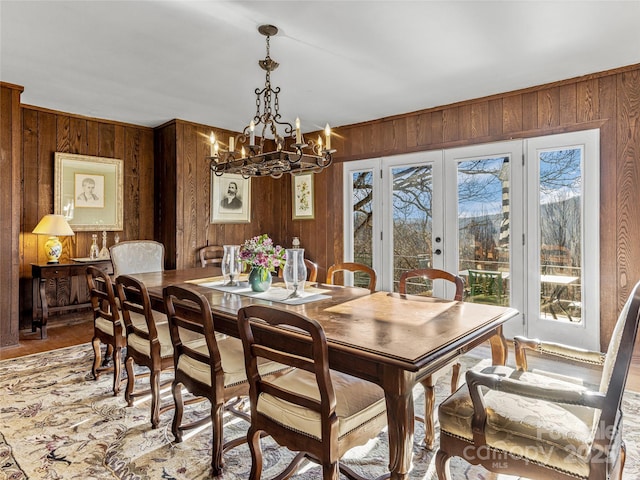 dining room with wood walls, an inviting chandelier, and french doors