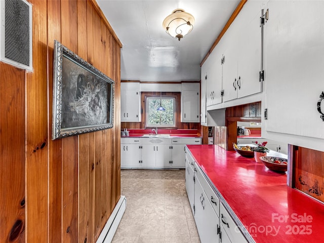 kitchen with sink, crown molding, wooden walls, white cabinetry, and baseboard heating