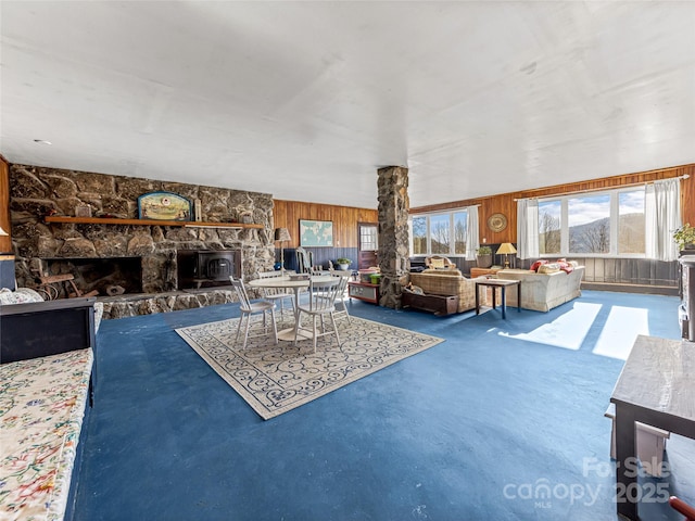 living room with carpet floors, wood walls, and a stone fireplace