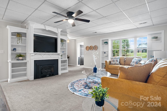 living room with light carpet, built in features, a drop ceiling, and ceiling fan