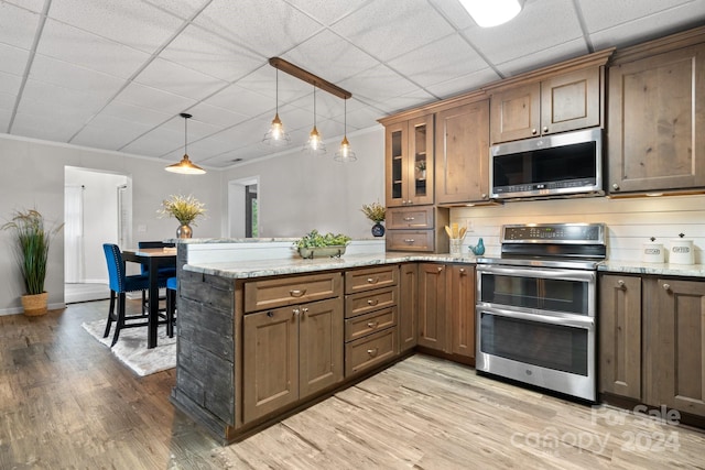 kitchen featuring stainless steel appliances, pendant lighting, light stone counters, and light hardwood / wood-style floors