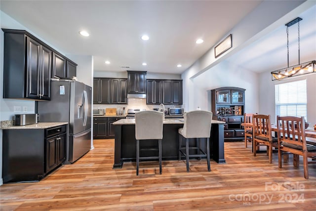 kitchen featuring appliances with stainless steel finishes, decorative light fixtures, light hardwood / wood-style floors, light stone countertops, and a center island