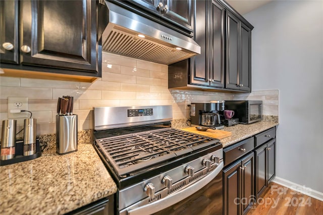 kitchen featuring decorative backsplash, stove, light wood-type flooring, and light stone countertops