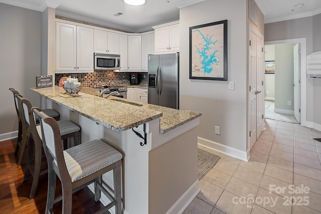 kitchen with kitchen peninsula, stainless steel appliances, white cabinetry, and light stone countertops