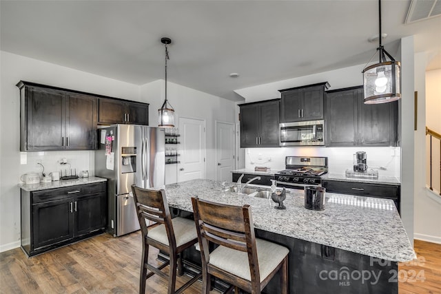 kitchen with decorative backsplash, a center island with sink, stainless steel appliances, and hardwood / wood-style floors