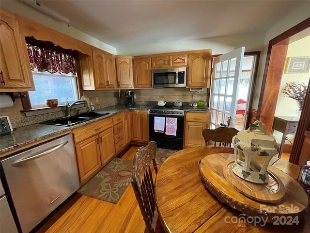 kitchen featuring brown cabinets, stainless steel appliances, dark countertops, a sink, and light wood-type flooring