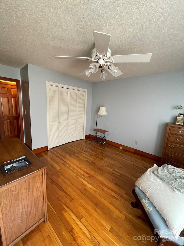 bedroom featuring a closet, ceiling fan, a textured ceiling, wood finished floors, and baseboards