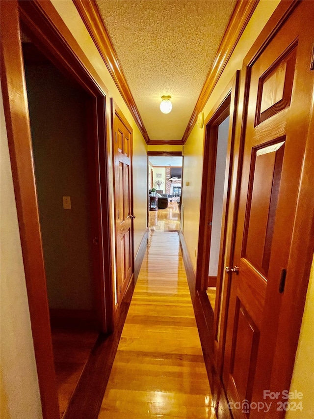 hallway featuring a textured ceiling, light wood-style floors, baseboards, and crown molding