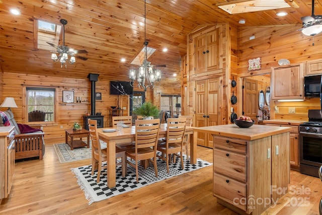 dining room with light hardwood / wood-style flooring, wooden walls, lofted ceiling with skylight, wood ceiling, and a wood stove