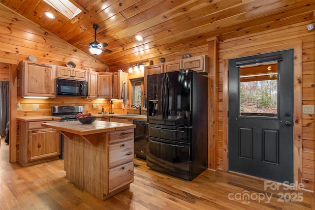 kitchen with tile counters, light hardwood / wood-style flooring, wood walls, black appliances, and a kitchen island