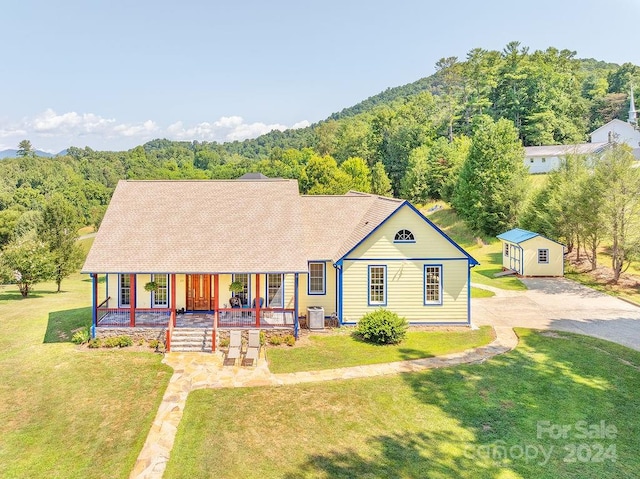 view of front of home featuring covered porch, a front yard, central AC, and a shed