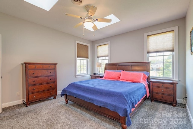 carpeted bedroom with ceiling fan, a skylight, and multiple windows