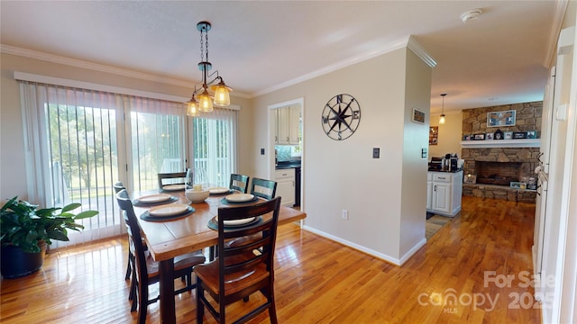 dining room featuring light wood-type flooring, crown molding, and a stone fireplace