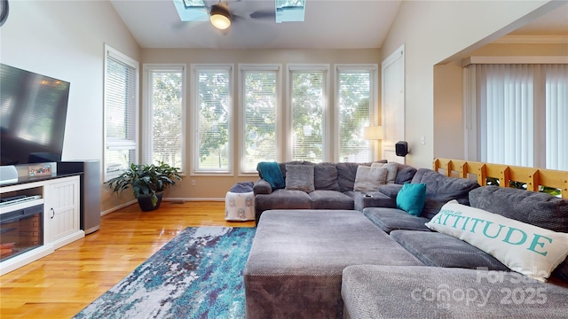 living room with ceiling fan, vaulted ceiling with skylight, and wood-type flooring