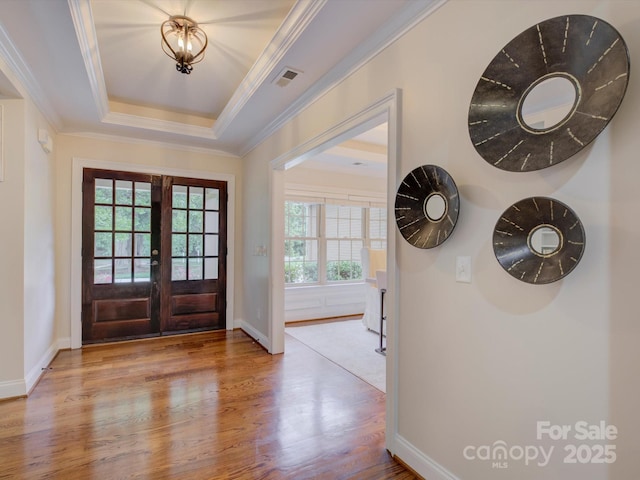 foyer entrance featuring french doors, light wood-type flooring, a tray ceiling, and ornamental molding