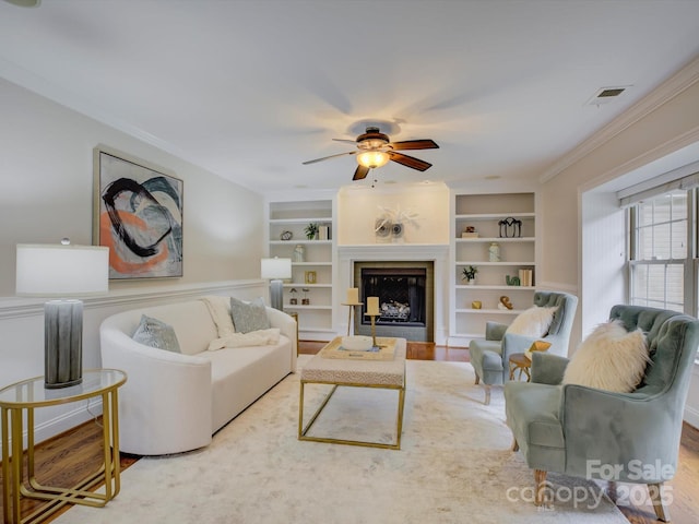 living room featuring built in shelves, ceiling fan, and ornamental molding