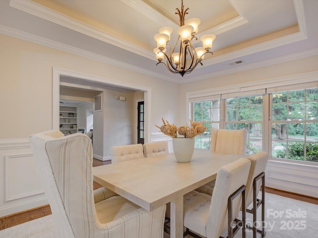 dining area featuring a raised ceiling, plenty of natural light, a chandelier, and light wood-type flooring