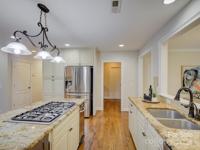 kitchen featuring sink, stainless steel appliances, light stone counters, light hardwood / wood-style floors, and decorative light fixtures