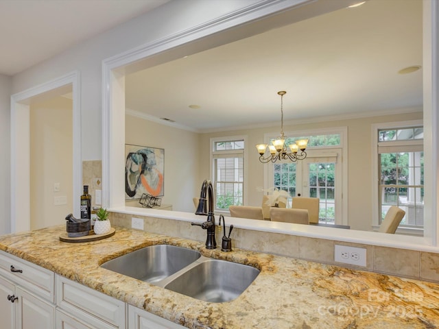 kitchen with sink, hanging light fixtures, light stone countertops, white cabinetry, and a chandelier