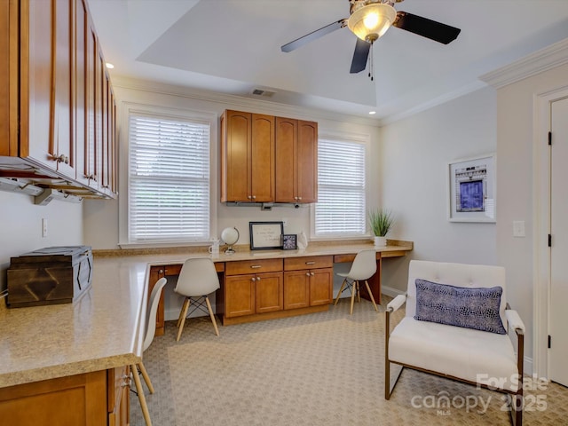 carpeted office with a raised ceiling, a wealth of natural light, built in desk, and ornamental molding