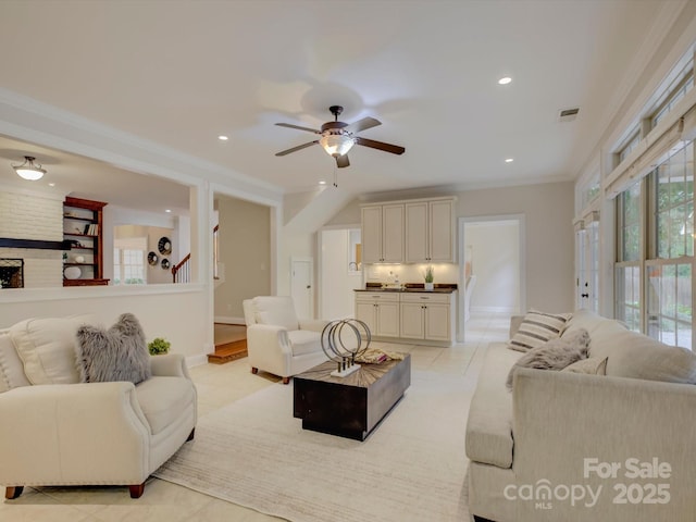 tiled living room featuring a fireplace, ceiling fan, and crown molding