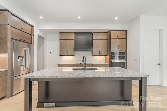 kitchen featuring light wood-type flooring, backsplash, premium range hood, appliances with stainless steel finishes, and light stone countertops