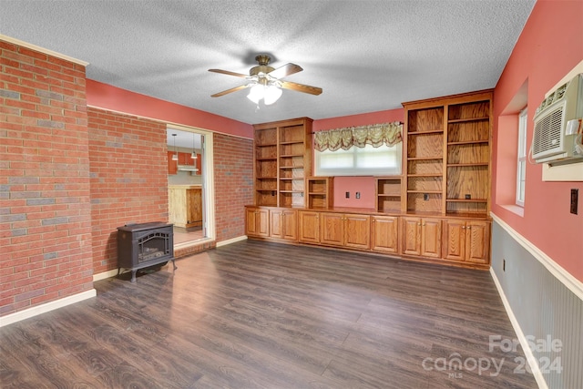 unfurnished living room with a textured ceiling, ceiling fan, brick wall, a wood stove, and dark hardwood / wood-style flooring