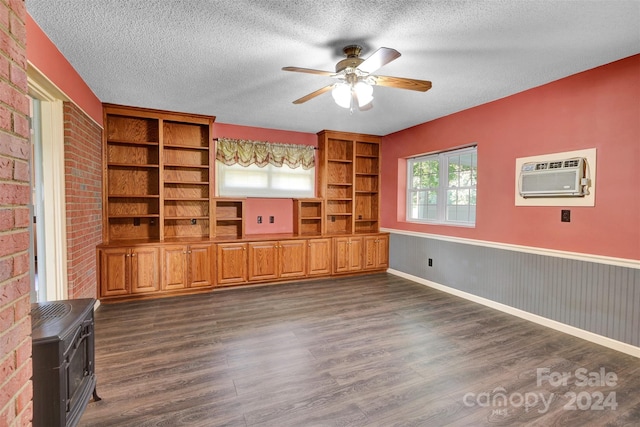 unfurnished living room with dark wood-type flooring, a textured ceiling, ceiling fan, a wood stove, and brick wall