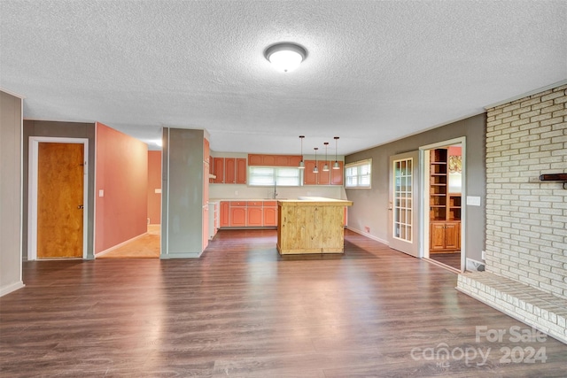 unfurnished living room with dark wood-type flooring, sink, a textured ceiling, and brick wall