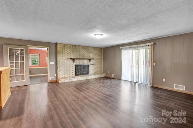 unfurnished living room with wood-type flooring, a textured ceiling, plenty of natural light, and a brick fireplace