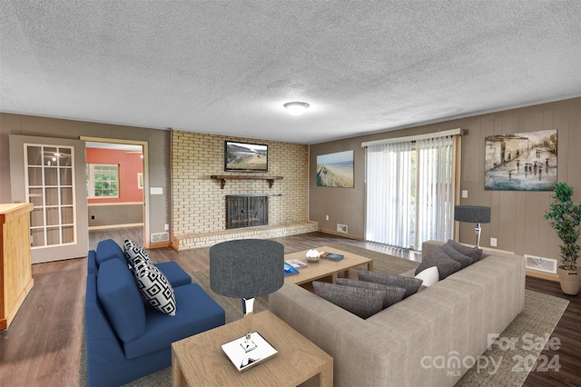 living room featuring a brick fireplace, brick wall, a textured ceiling, and dark hardwood / wood-style floors