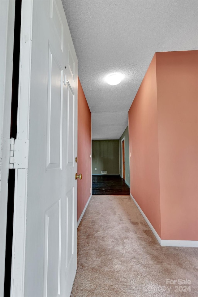 hall with a textured ceiling and light colored carpet