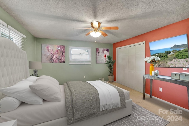 bedroom with a textured ceiling, light colored carpet, a closet, and ceiling fan