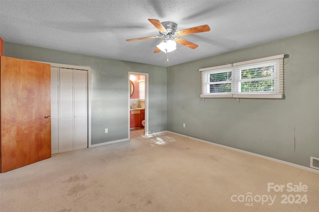 unfurnished bedroom with ceiling fan, ensuite bath, a textured ceiling, and light colored carpet