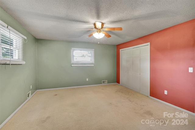 unfurnished bedroom featuring ceiling fan, light colored carpet, multiple windows, and a closet