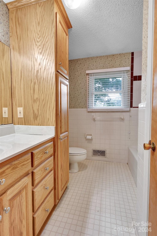 full bathroom with a textured ceiling, toilet, tile patterned flooring, tile walls, and vanity