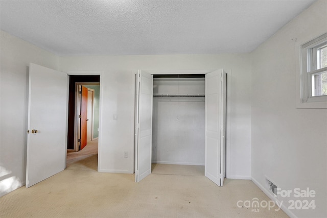 unfurnished bedroom with a closet, a textured ceiling, and light colored carpet