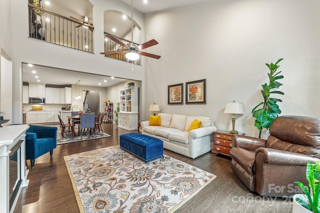 living room featuring ceiling fan, dark wood-type flooring, and a towering ceiling