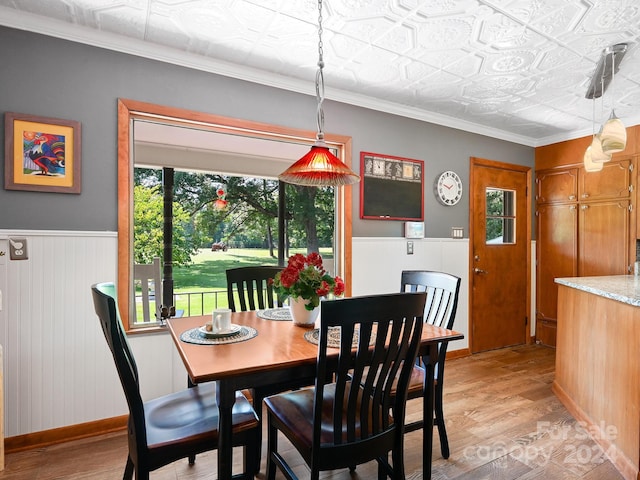 dining area with crown molding, light hardwood / wood-style flooring, wood walls, and a wealth of natural light