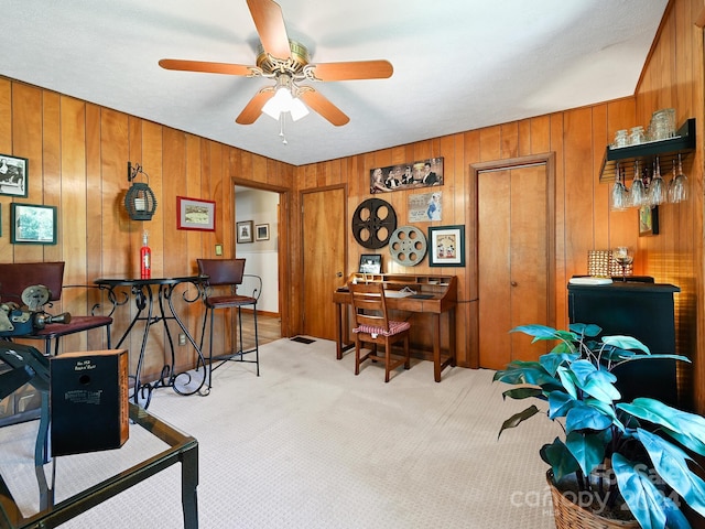 home office with wood walls, ceiling fan, and light carpet