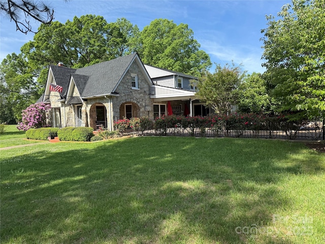 tudor home with a front lawn, a chimney, stone siding, and fence