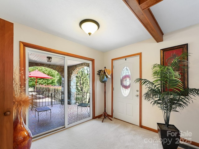 entryway with beamed ceiling, light carpet, and baseboards